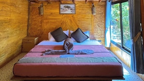 Una habitación de madera con una cama, un cuadro en la pared y una ventana con cortinas.