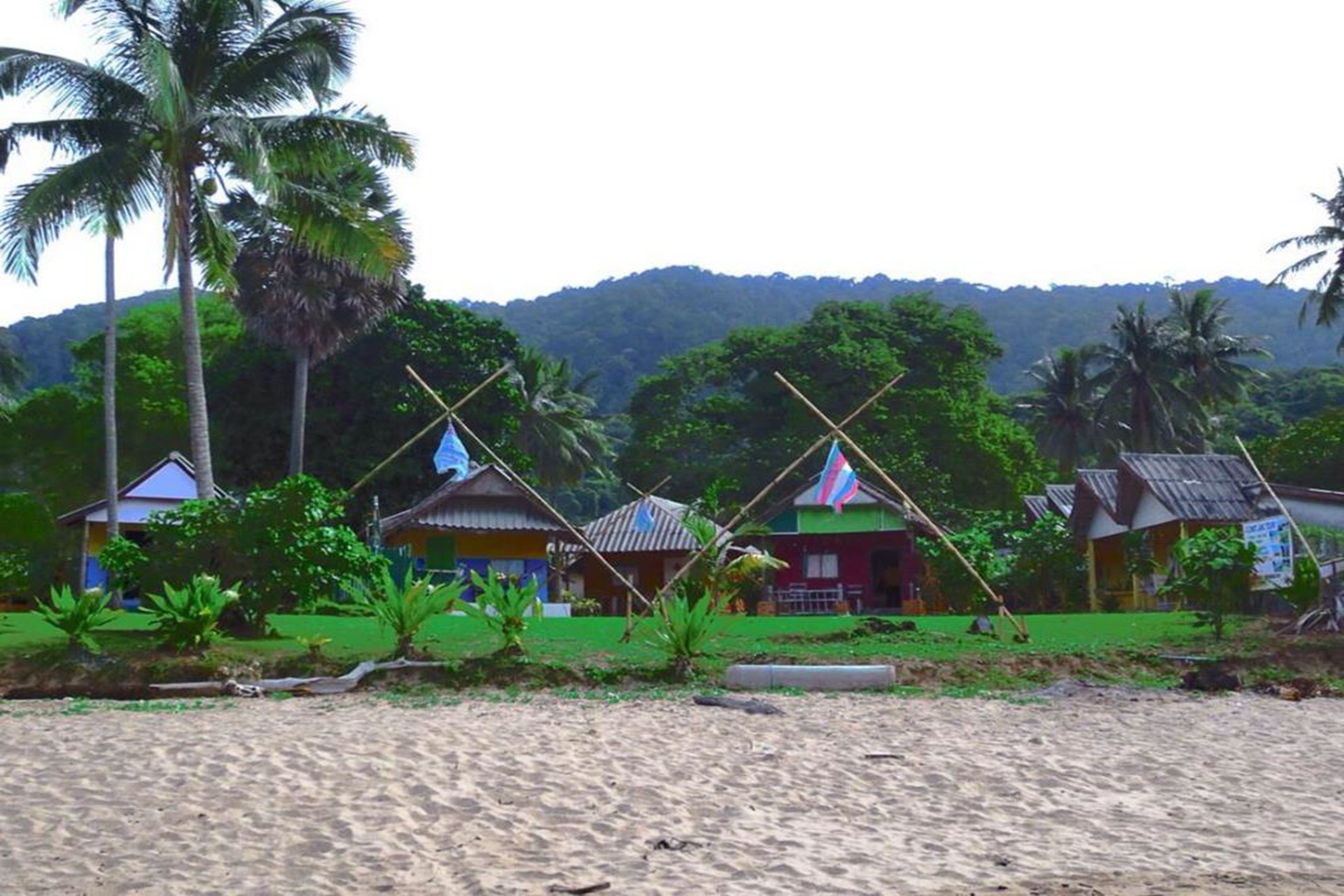Un resort frente a la playa con cabañas sencillas y coloridas, y palmeras.