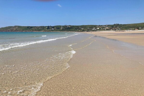Ein Strand mit klarem Wasser, sanften Wellen und einer entfernten Ansicht von Häusern auf einem Hügel.