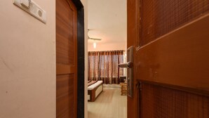 A hallway leading to a bedroom with a bed, a bedside table, and a ceiling fan. - Hotel Sai Shraddha (Rahata)