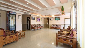 A spacious lobby with wooden furniture, a Pepsi refrigerator, framed pictures on the walls, and a television. - Hotel Sai Shraddha (Rahata)