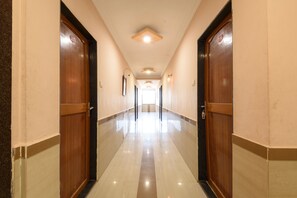 A corridor with wooden doors and a tiled floor, leading to a bright area at the end.