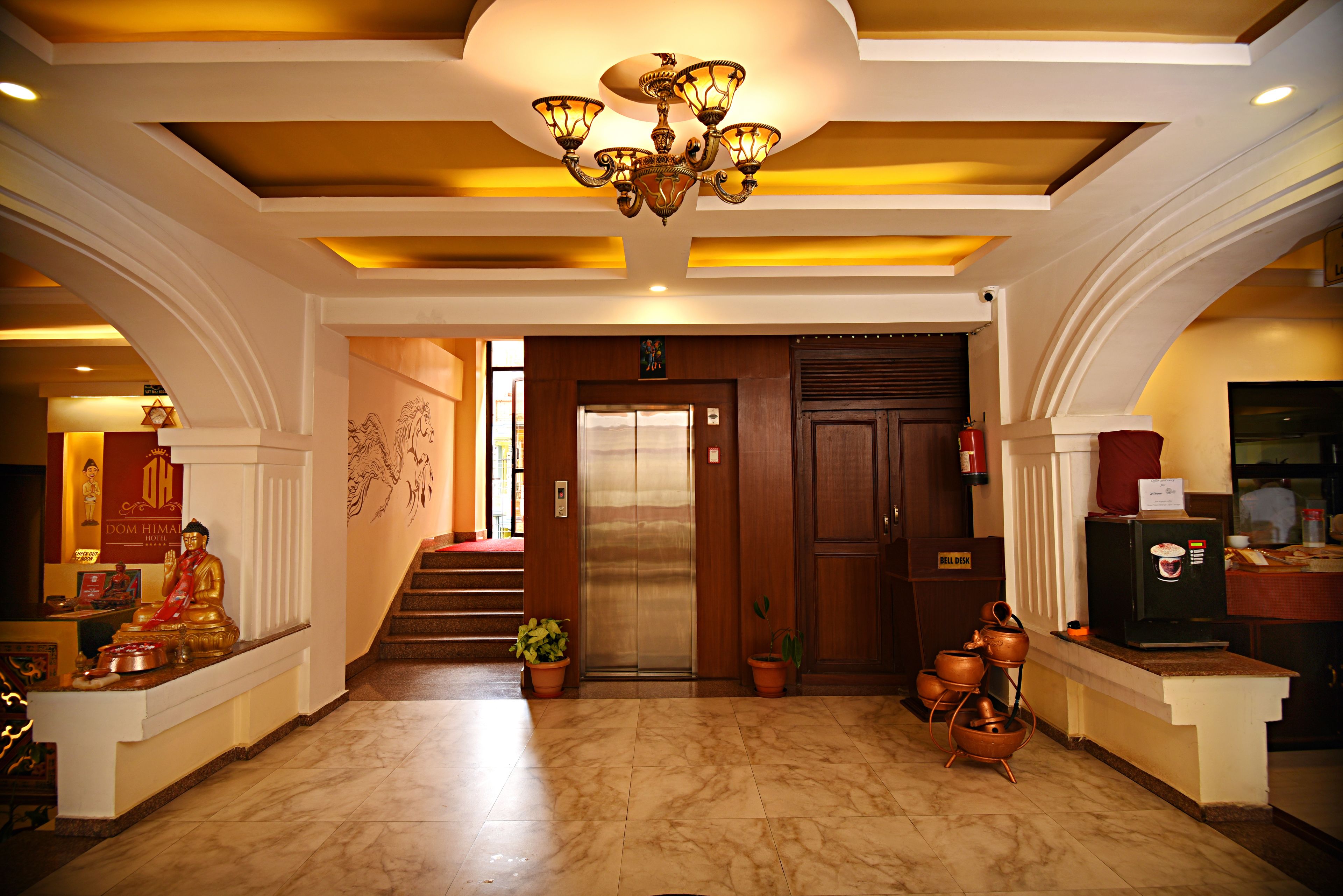 A hotel lobby with a marble floor, a Buddha statue, a staircase, and a reception desk.