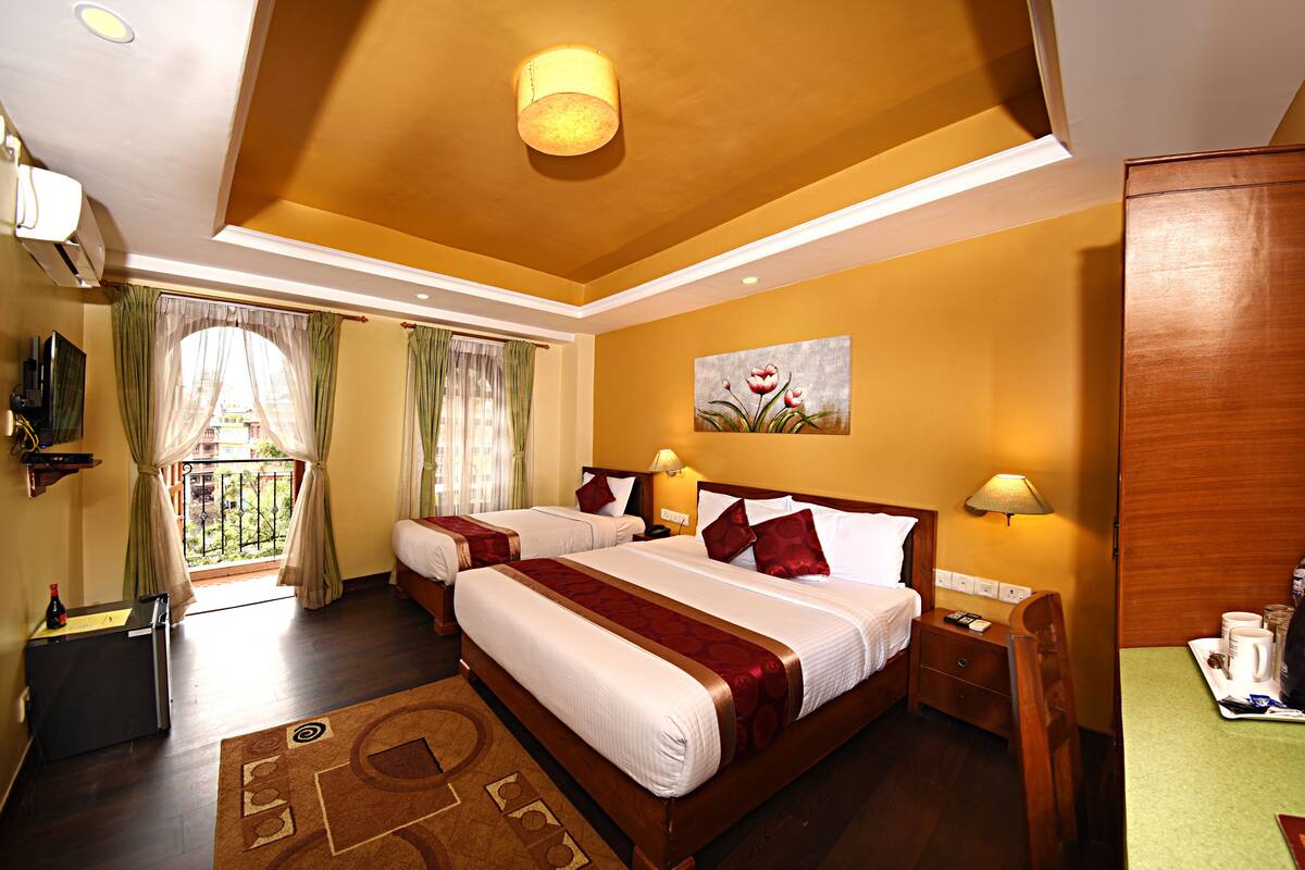 A hotel room with a large bed, two bedside tables, a desk with a chair, a painting on the wall, and a balcony with curtains.