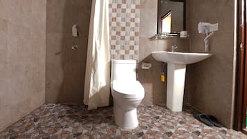 Un baño con piso de baldosas, inodoro, lavamanos y cortina de ducha.