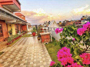 A paved pathway leading to a building with a red facade, surrounded by potted plants and flowers. - DOM Himalaya Hotel (Kathmandu)