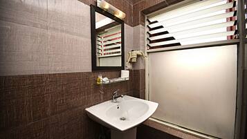 Un baño con lavamanos, espejo y ventana con persianas.