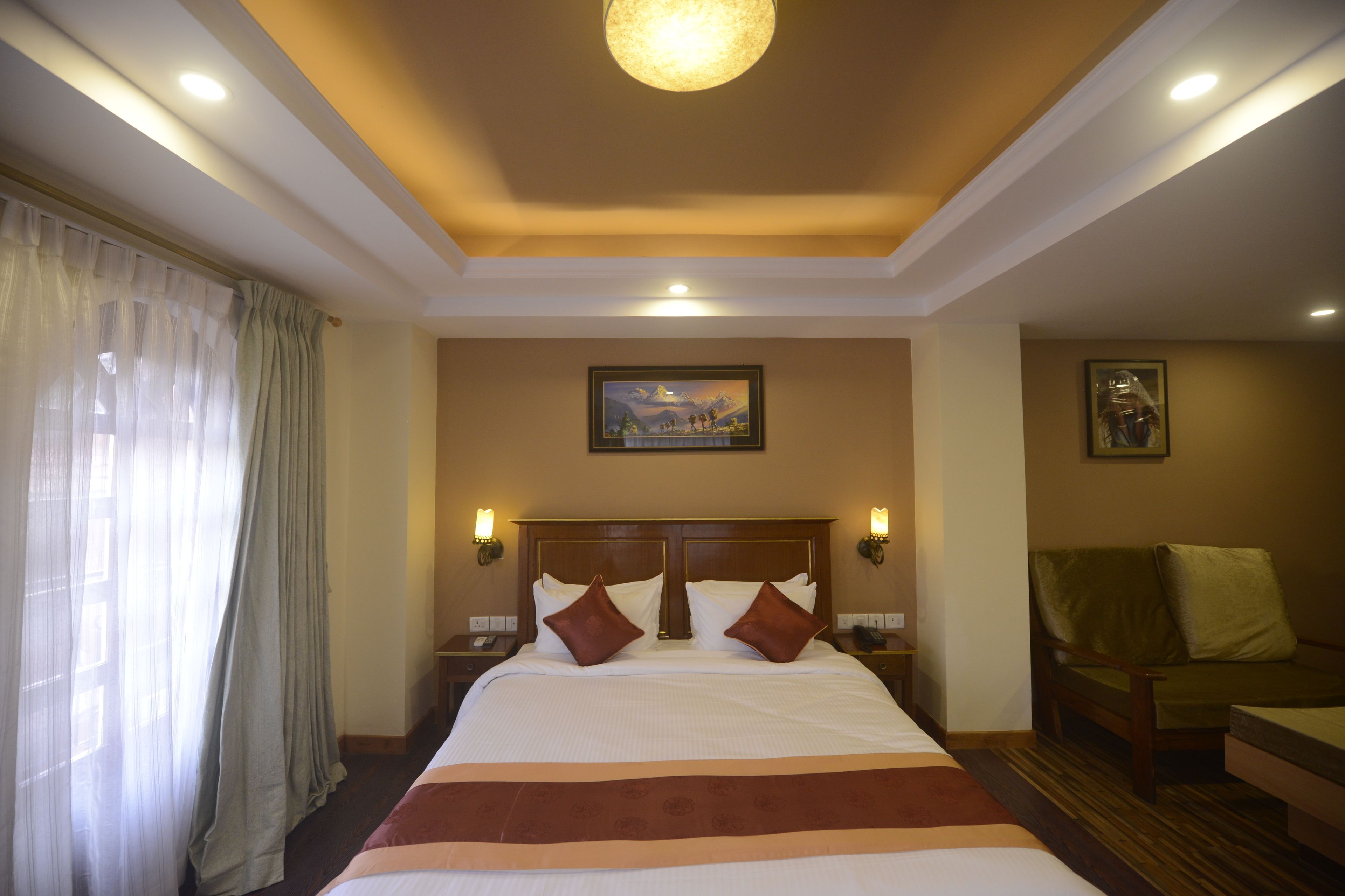 A hotel room with a large bed, two bedside tables, a nightstand, a sofa, and a painting on the wall.