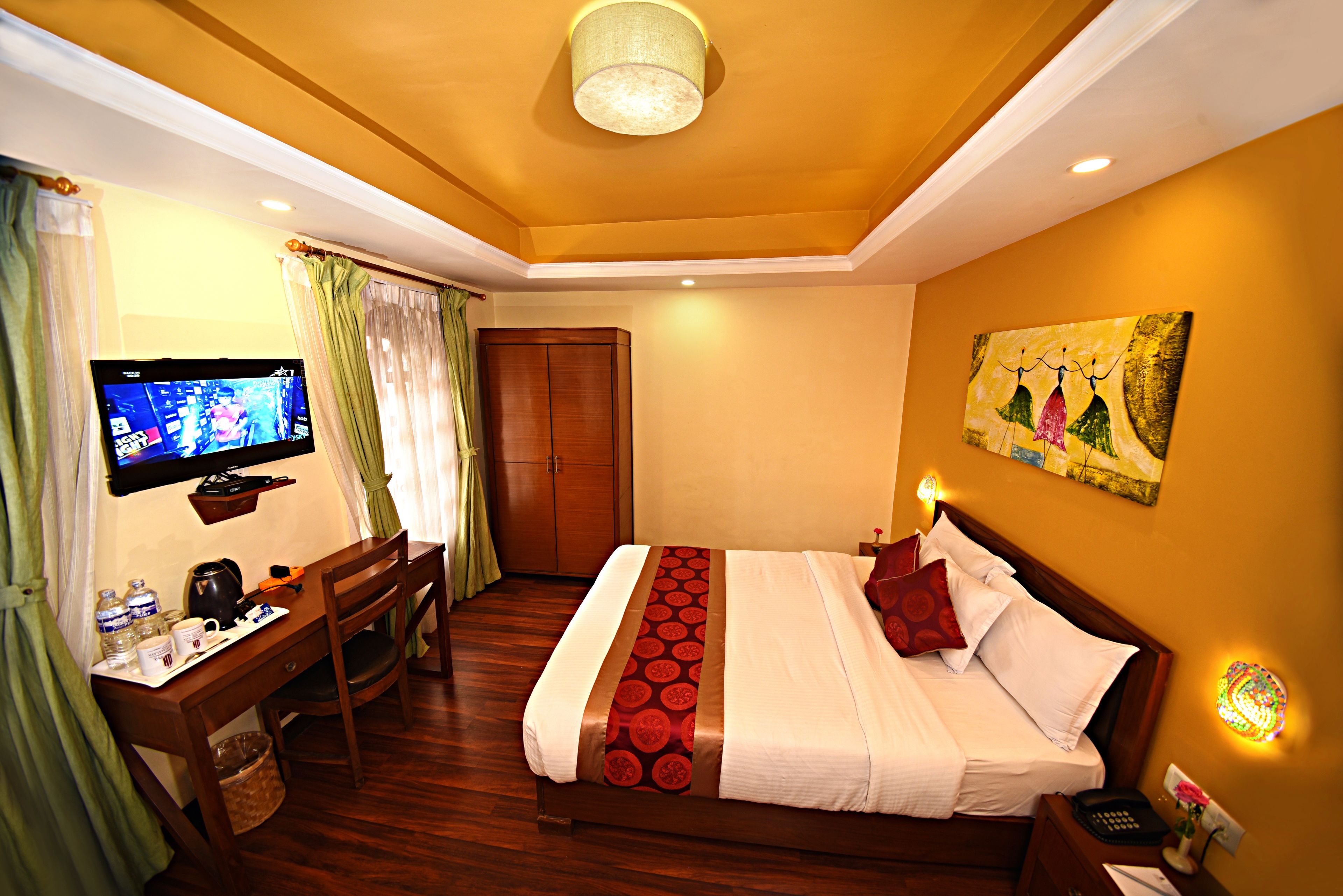 A hotel room with a bed, a desk, a television, and a painting on the wall.