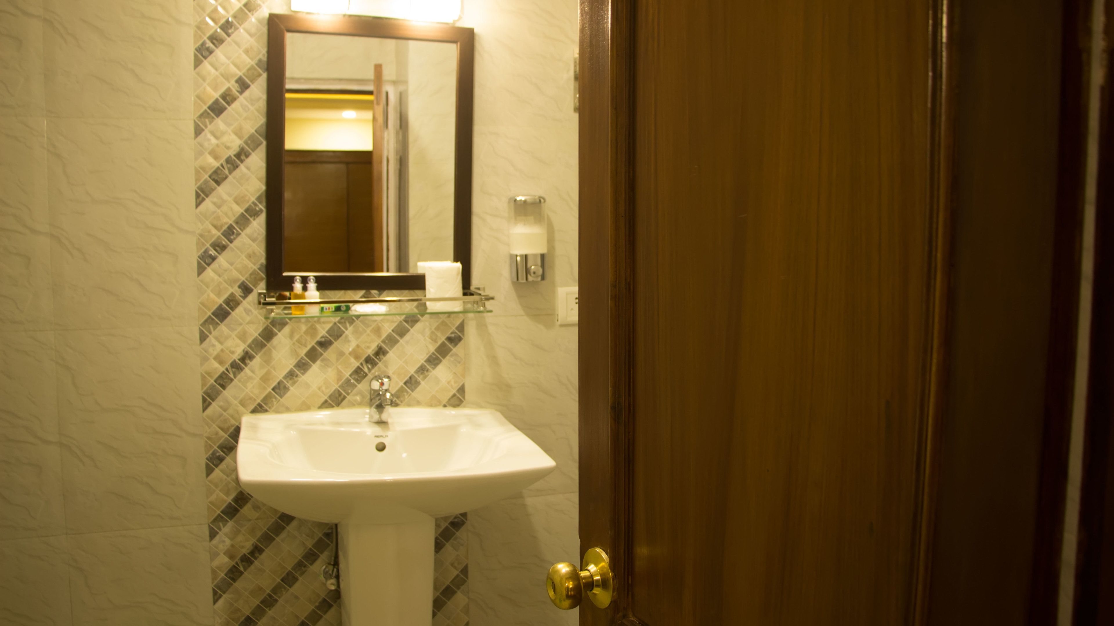 Une salle de bain avec un lavabo blanc, un miroir et une porte.
