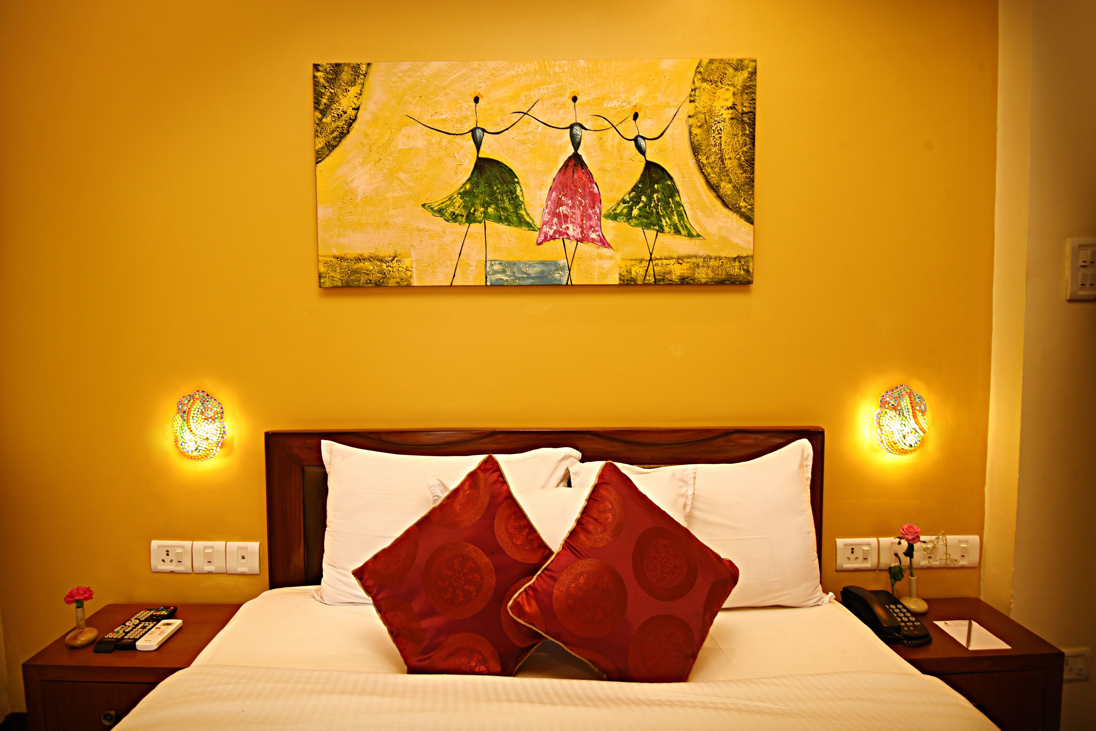 A hotel room with a bed, two nightstands, a painting, and wall sconces.