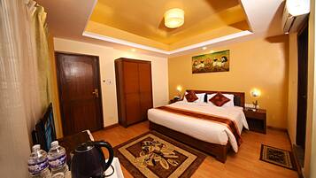 A hotel room with a bed, bedside tables, a desk with a kettle, and a painting on the wall.