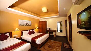 A hotel room with two beds, a desk, a television, and a painting on the wall.