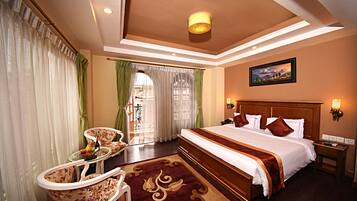 A hotel room with a large bed, a sitting area with a table and chairs, and a view of the outdoors through a window.