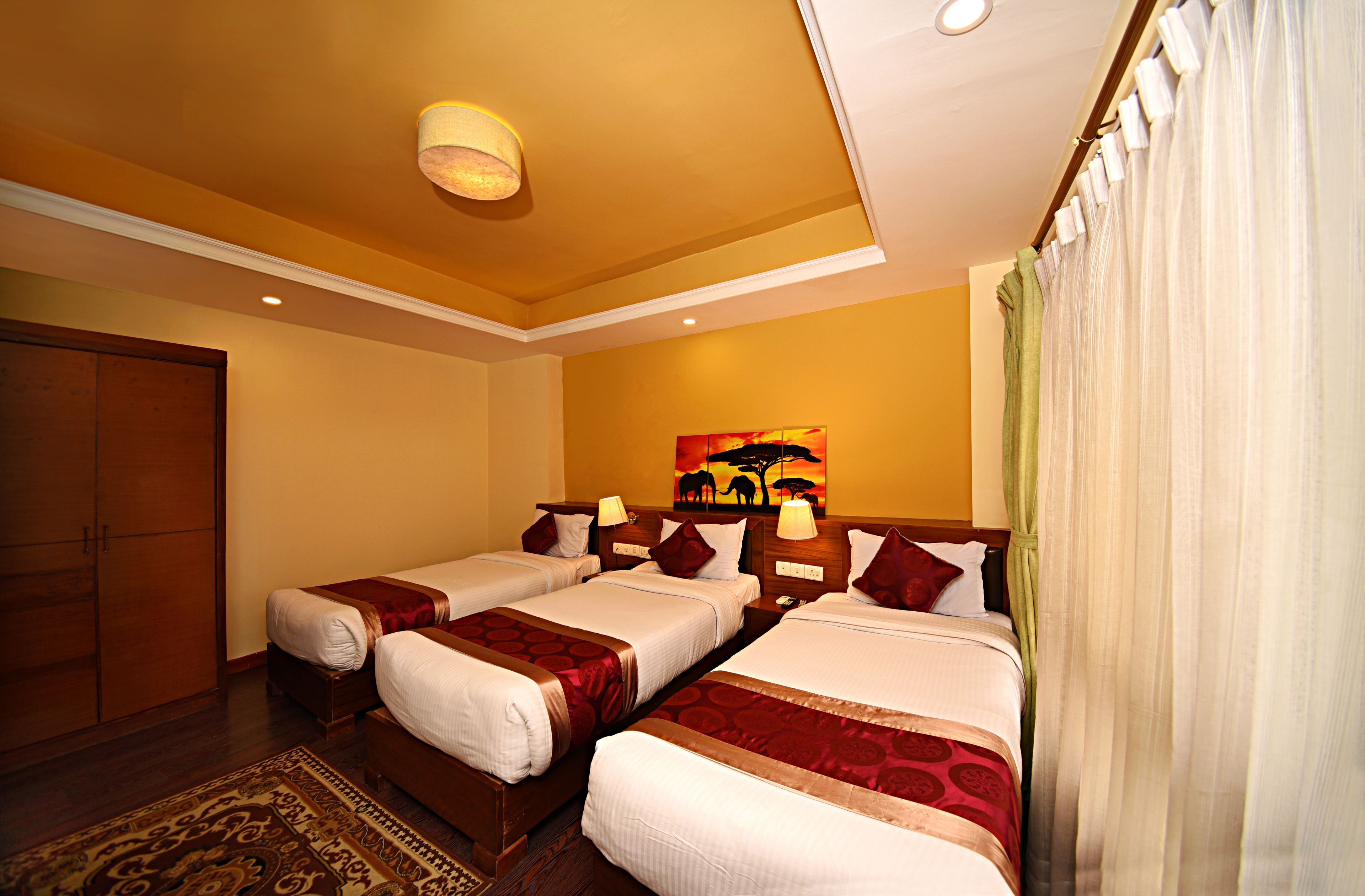 A hotel room with two single beds, a wooden wardrobe, a painting on the wall, and a patterned rug.