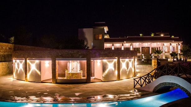 A modern hotel with a swimming pool, a covered outdoor area with seating, and a staircase leading to the entrance.