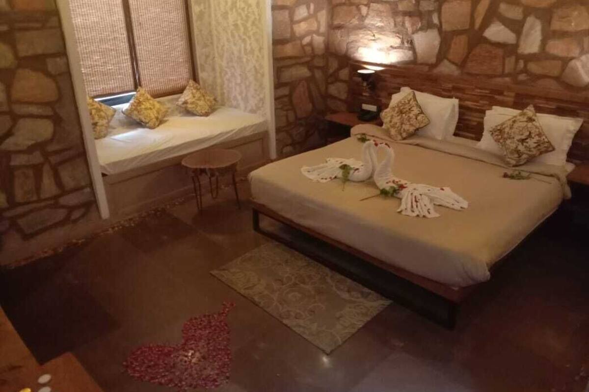 Un dormitorio con pared de piedra, una cama con sábanas blancas y una mesita con lámpara.