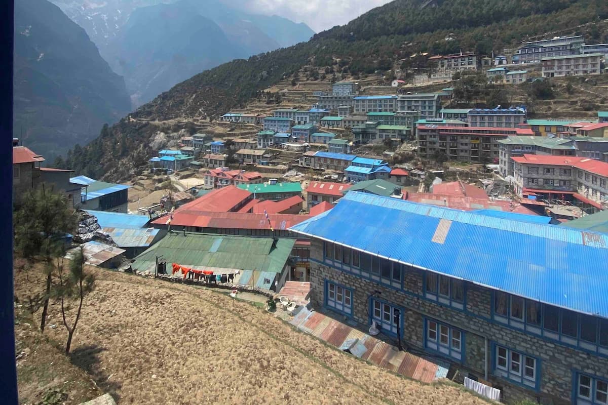 A mountainous village with colorful buildings, a clear sky, and distant snow-capped peaks.
