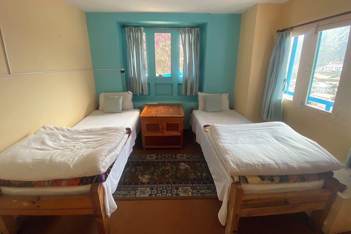 A room with two single beds, a small wooden table, and a window with curtains.
