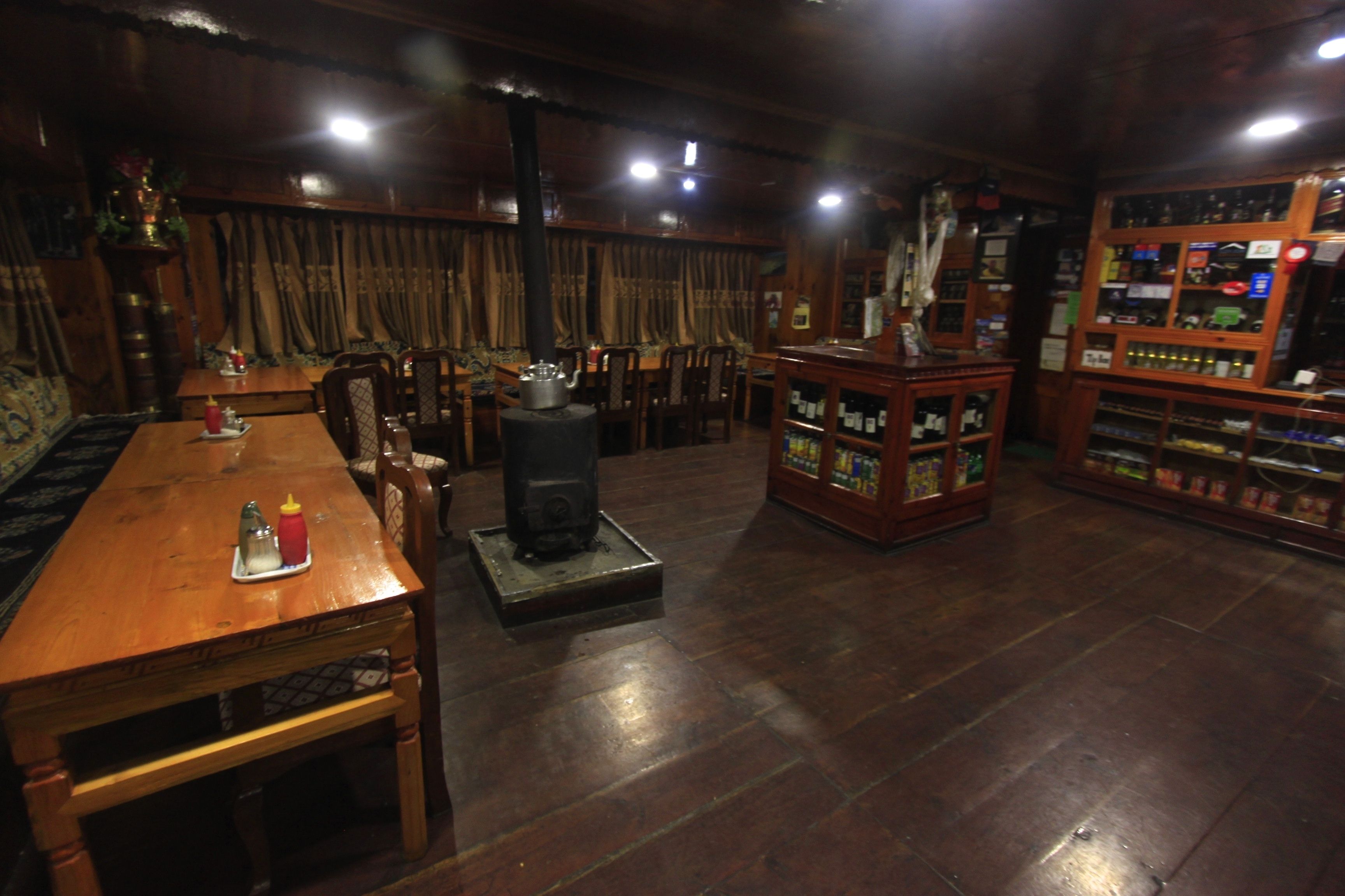 A wooden-floored room with a dining table, chairs, a speaker, and a shelf with various items.