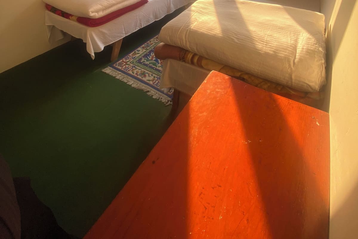 A small, compact room with two single beds, a green mat, and a wooden table.