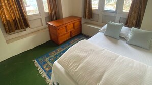 A bedroom with a bed, a wooden dresser, and a window with curtains. - Himalayan Lodge (Namche Bazar)