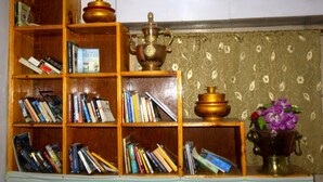 A wooden bookshelf filled with books and two brass tea pots. - Himalayan Lodge (Namche Bazar)
