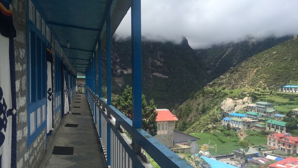 A corridor with blue railings, leading to a mountainous landscape with buildings. - Himalayan Lodge (Namche Bazar)