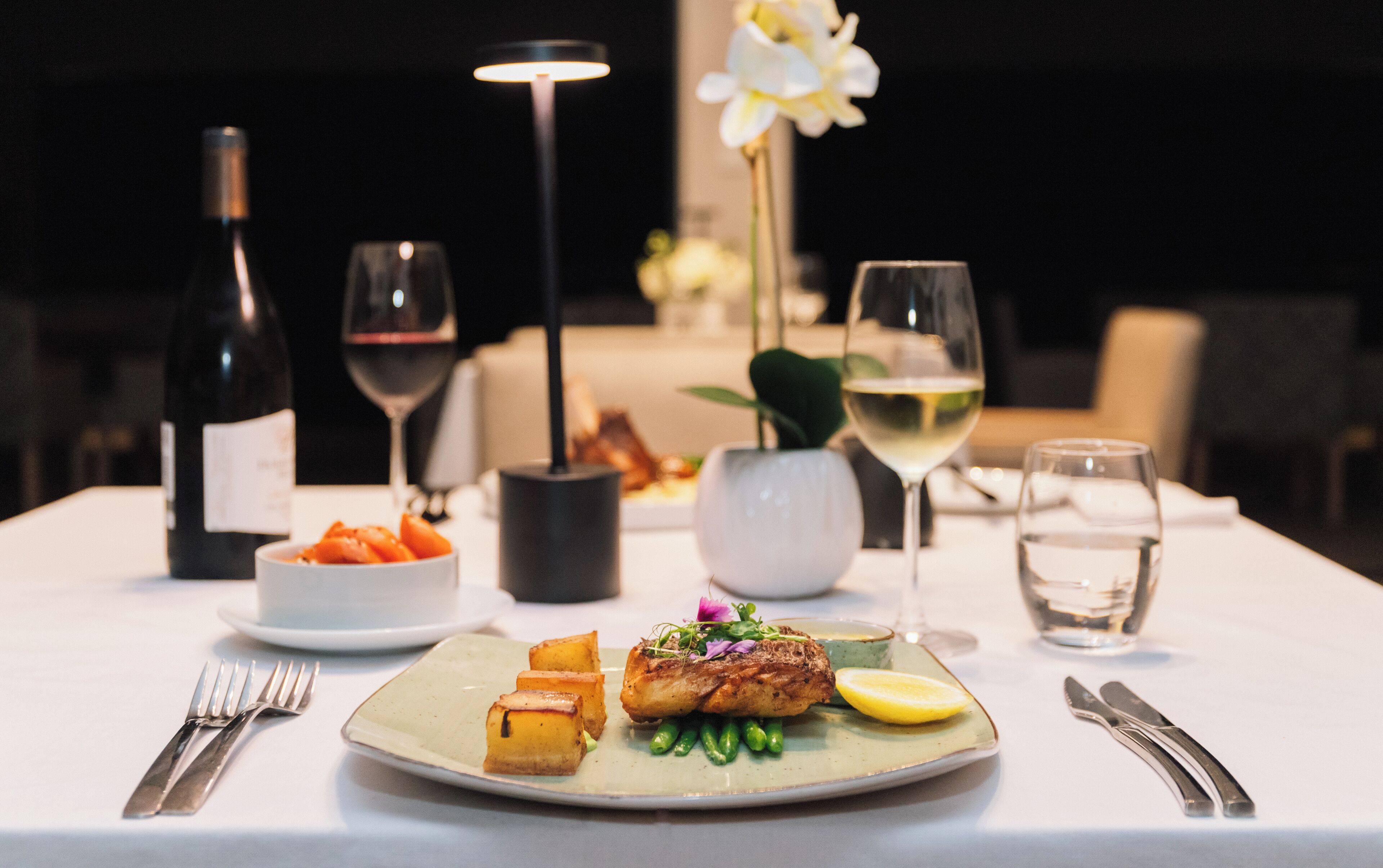 A dining table set with a plate of food, wine glasses, and cutlery.