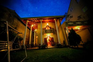A building with a covered patio, a central entrance, and a starry night sky above. - Frangipani Motel (Galle)