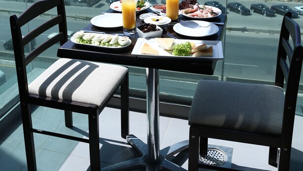 Una mesa con platos de comida y un vaso de jugo de naranja en un balcón con vista al mar.