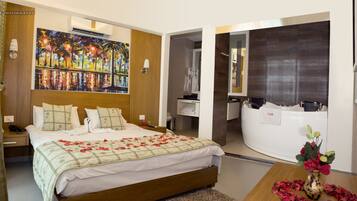 A modern hotel room with a large bed, a painting on the wall, a bathroom with a bathtub, and a small table with flowers.