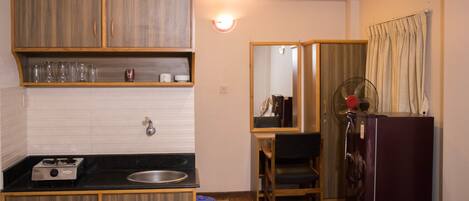 A compact hotel room with a kitchenette, a bed, a desk, and a mirror.