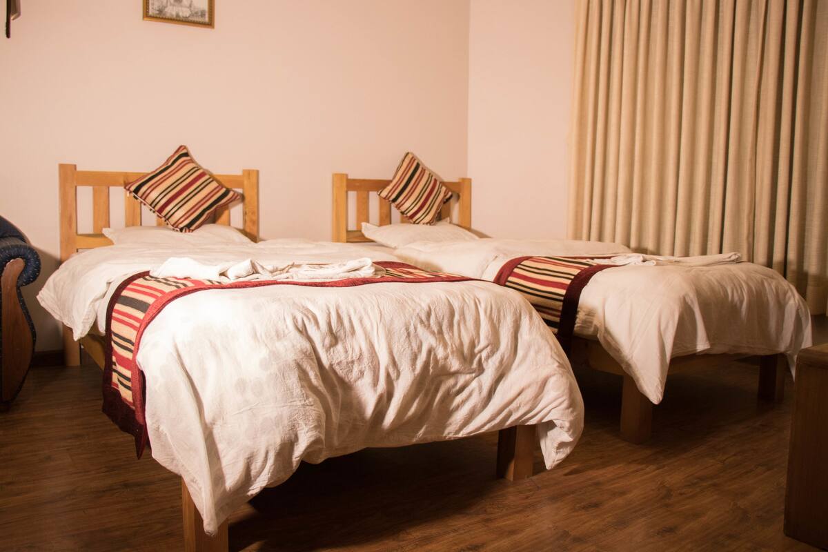 Quarto de hotel com duas camas de solteiro, cabeceiras de madeira e uma janela grande com cortinas.