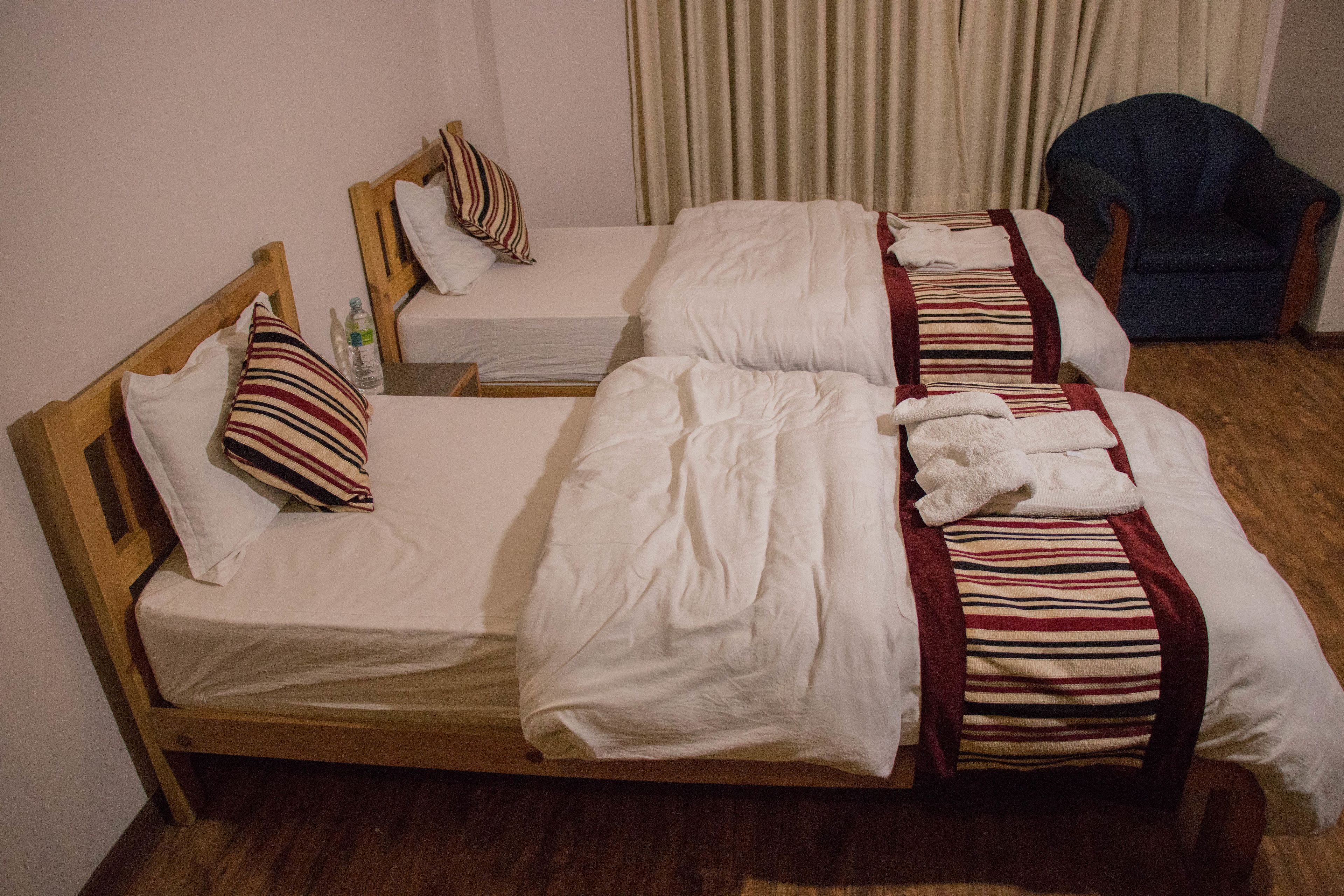 A hotel room with two single beds, wooden headboards, and a blue armchair.