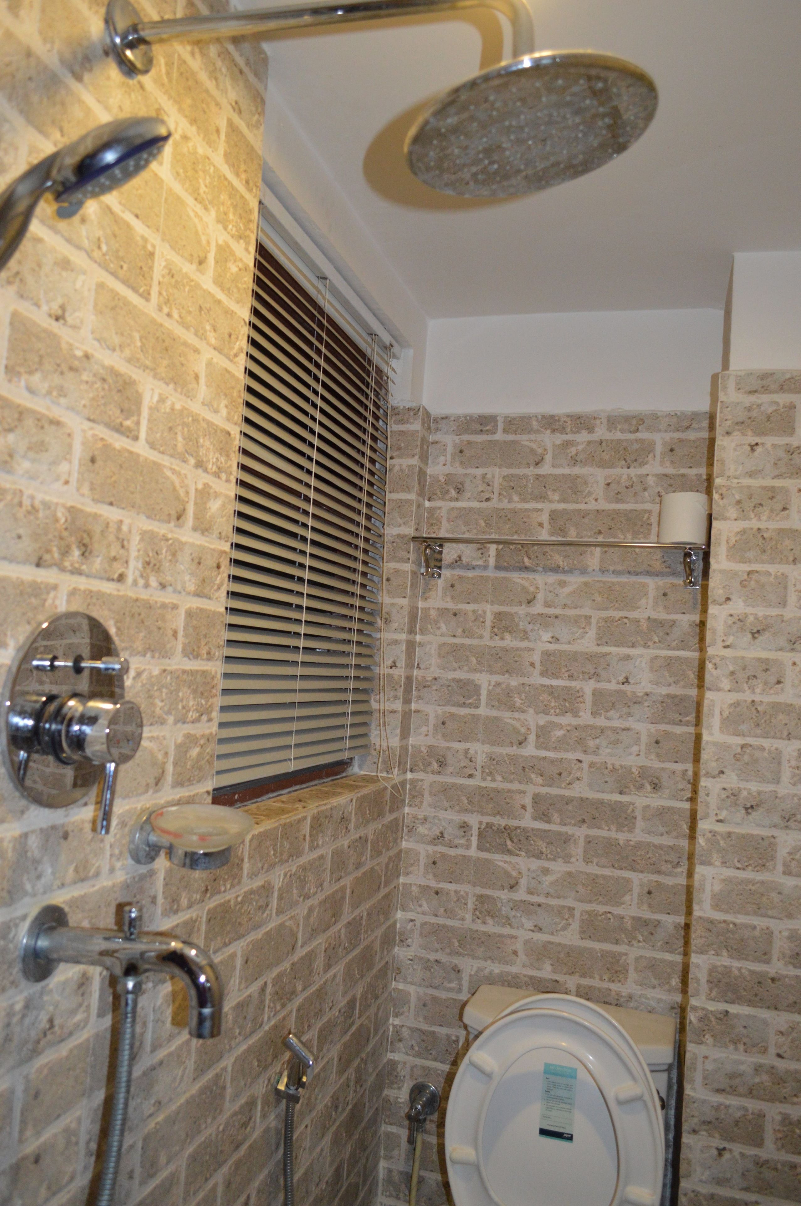 A bathroom with a shower, toilet, and a window with blinds.