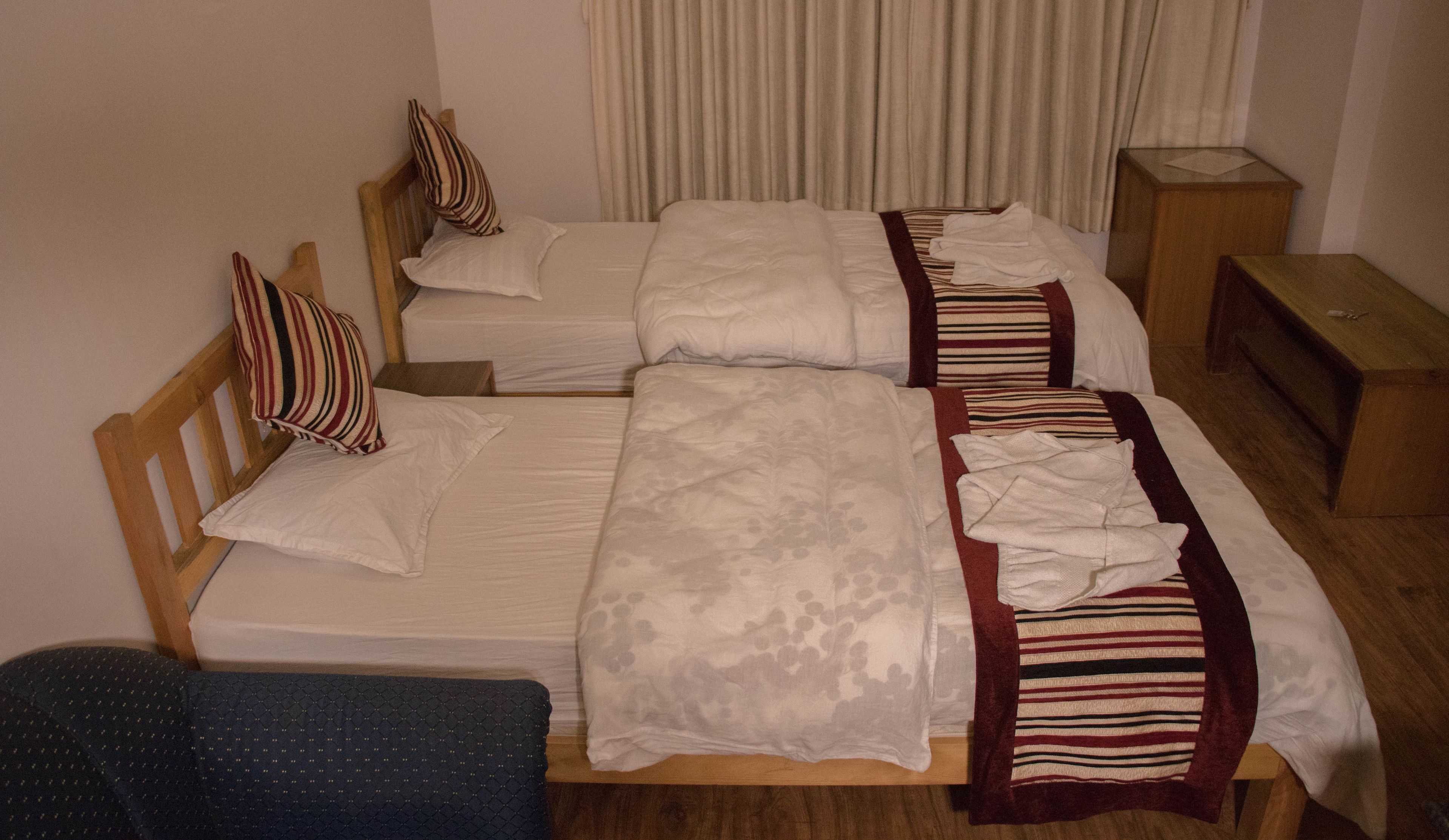 A hotel room with two single beds, a wooden headboard, a small wooden nightstand, and a blue chair.