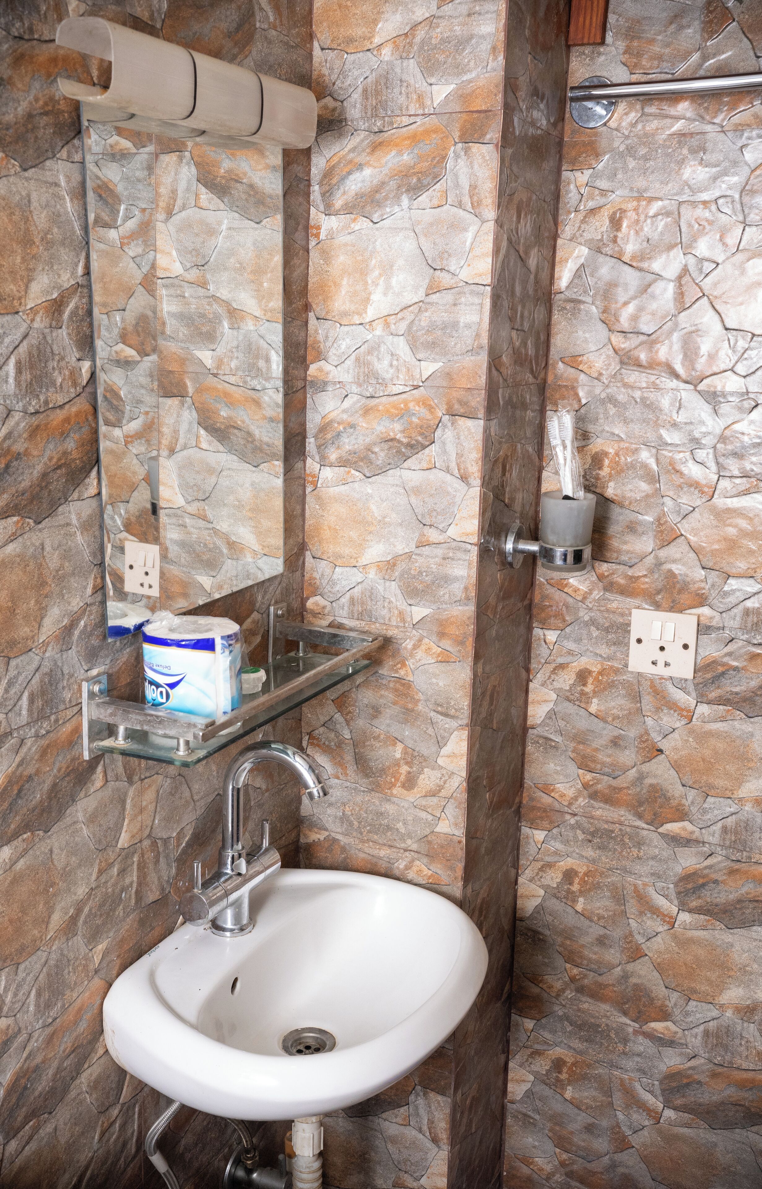 A bathroom with a stone wall, a white sink, a mirror, and a towel dispenser.