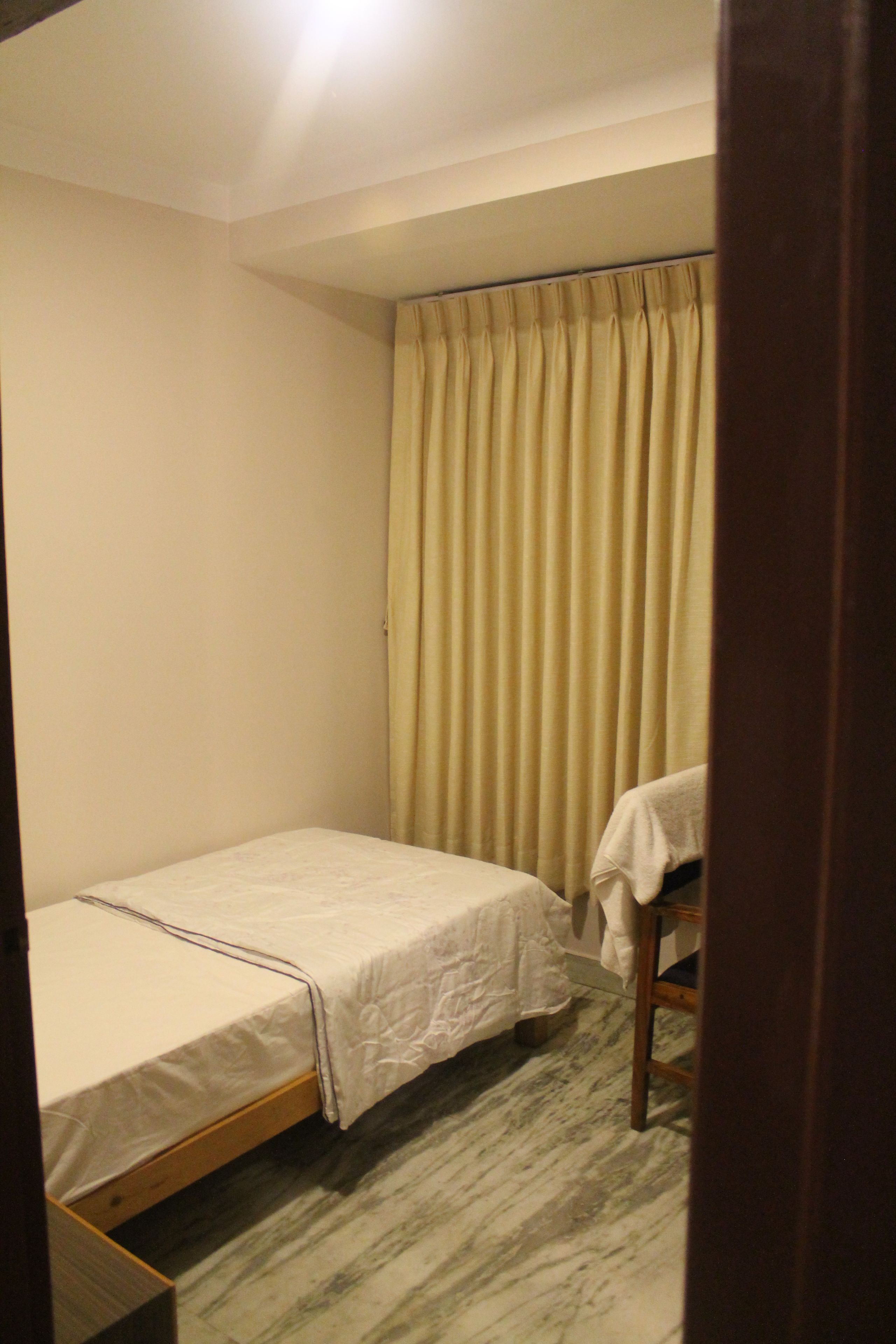 A small, single-bed room with a wooden floor, a curtain, and a chair.
