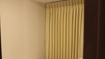 A small, single-bed room with a wooden floor, a curtain, and a chair.