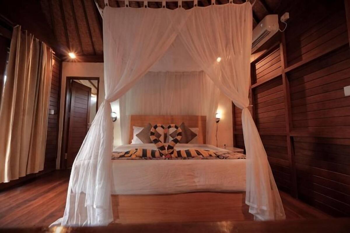 Een slaapkamer met een hemelbed, houten wanden en een nachtkastje met een lamp.