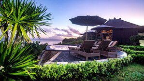 A poolside area with lounge chairs and umbrellas, surrounded by lush greenery and a view of the sea. - Bali Belva (Lembongan Island)