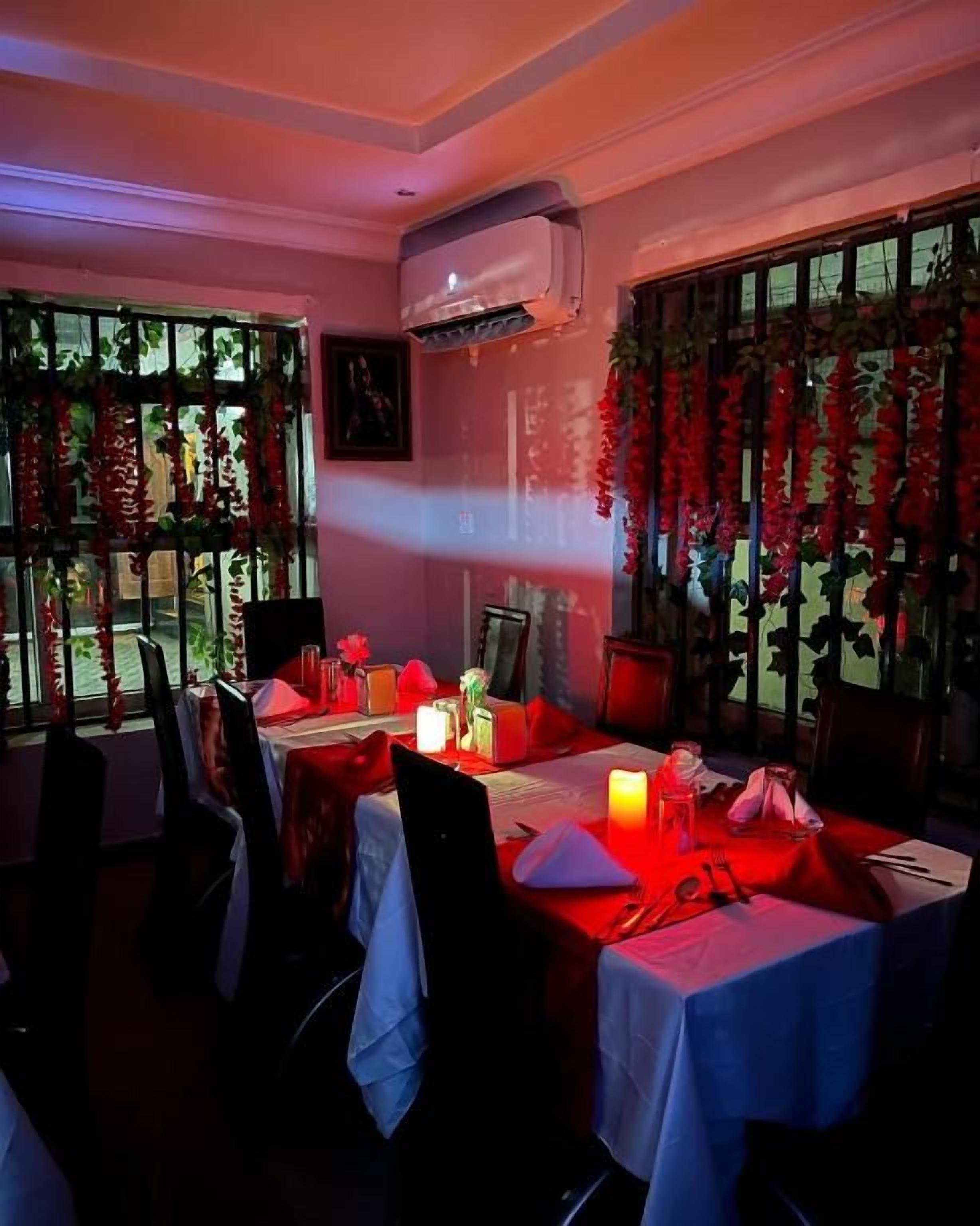 A dining area with tables set for two, chairs, and a window with decorative foliage.