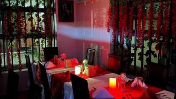 A dining area with tables set for two, chairs, and a window with decorative foliage.