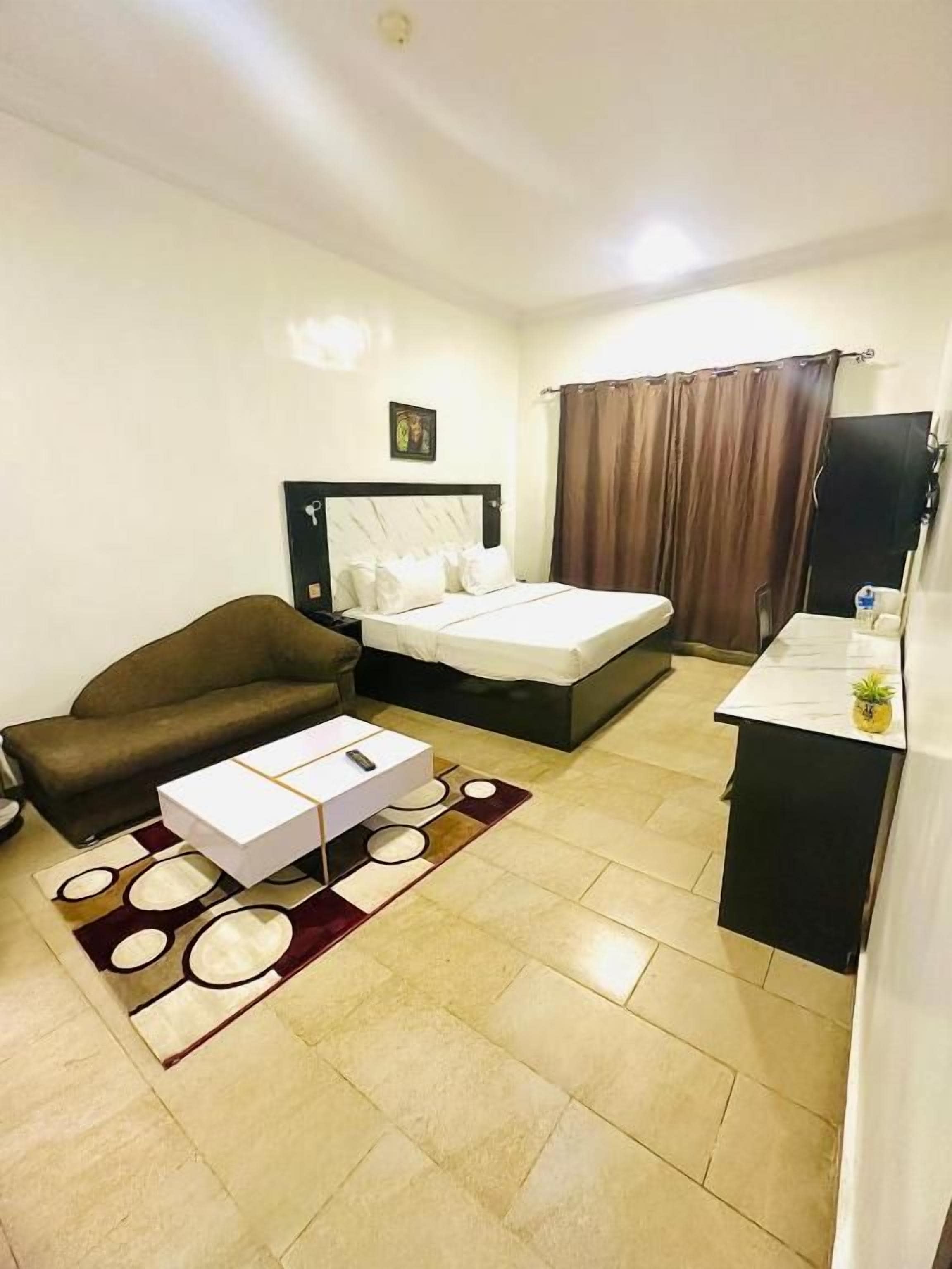 Una habitación de hotel con cama, sofá, mesa de centro, escritorio y cortina.