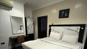 A modern bedroom with a large bed, a bedside table, a mirror, and a door. - Posh Apartments Metro (Lagos)