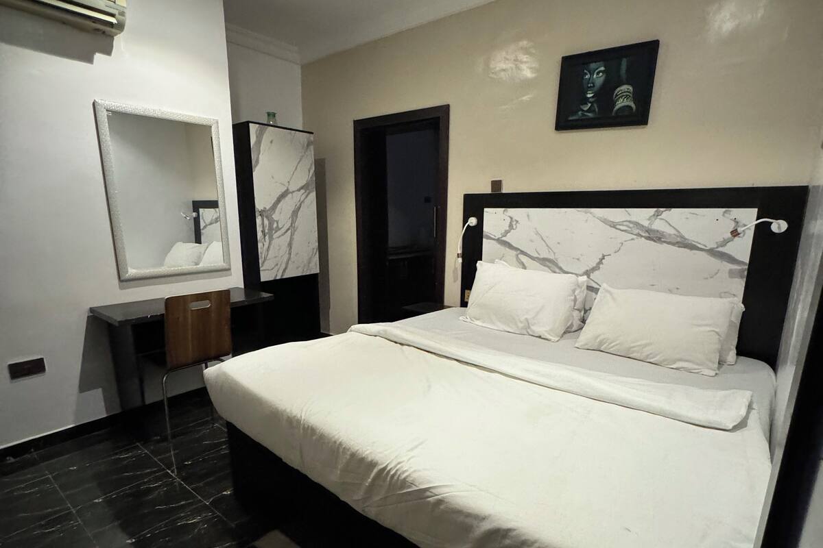 A modern bedroom with a large bed, a bedside table, a mirror, and a door.