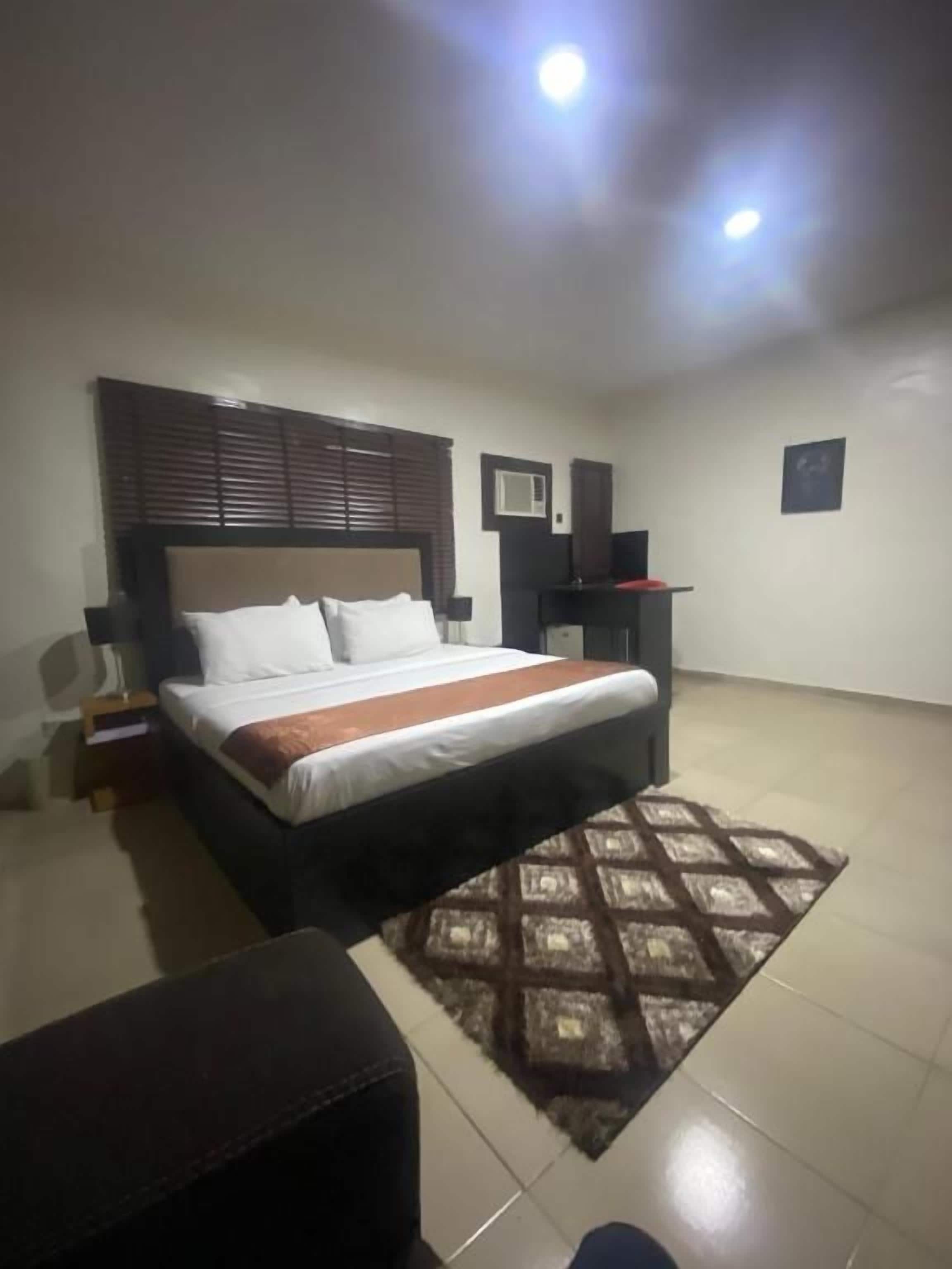 A bedroom with a bed, a bedside table, a nightstand, a rug, and a wall-mounted speaker.