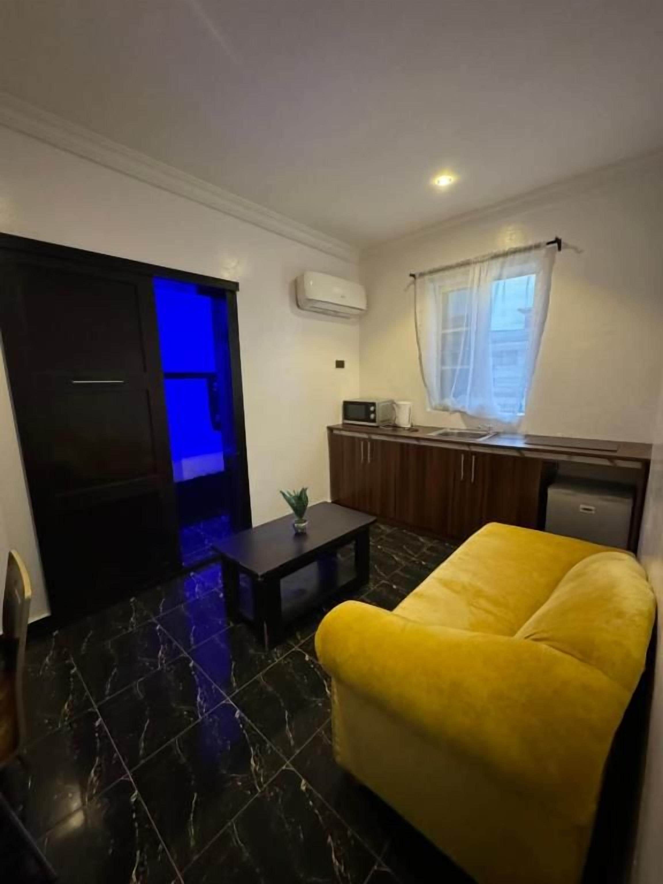 A compact living space with a yellow armchair, a small table, a microwave, and a window with curtains.