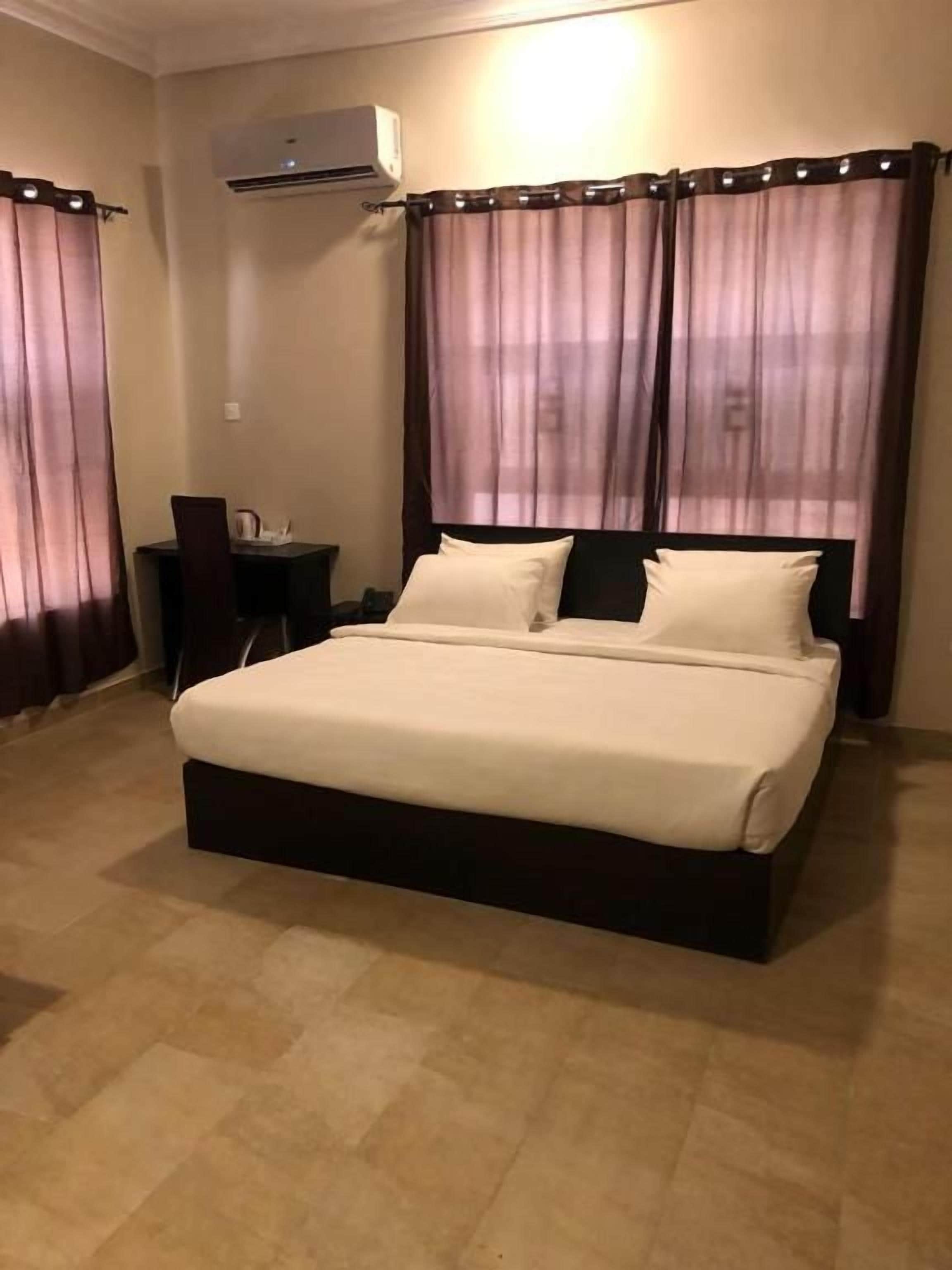 A hotel room with a large bed, a desk, and an air conditioning unit.